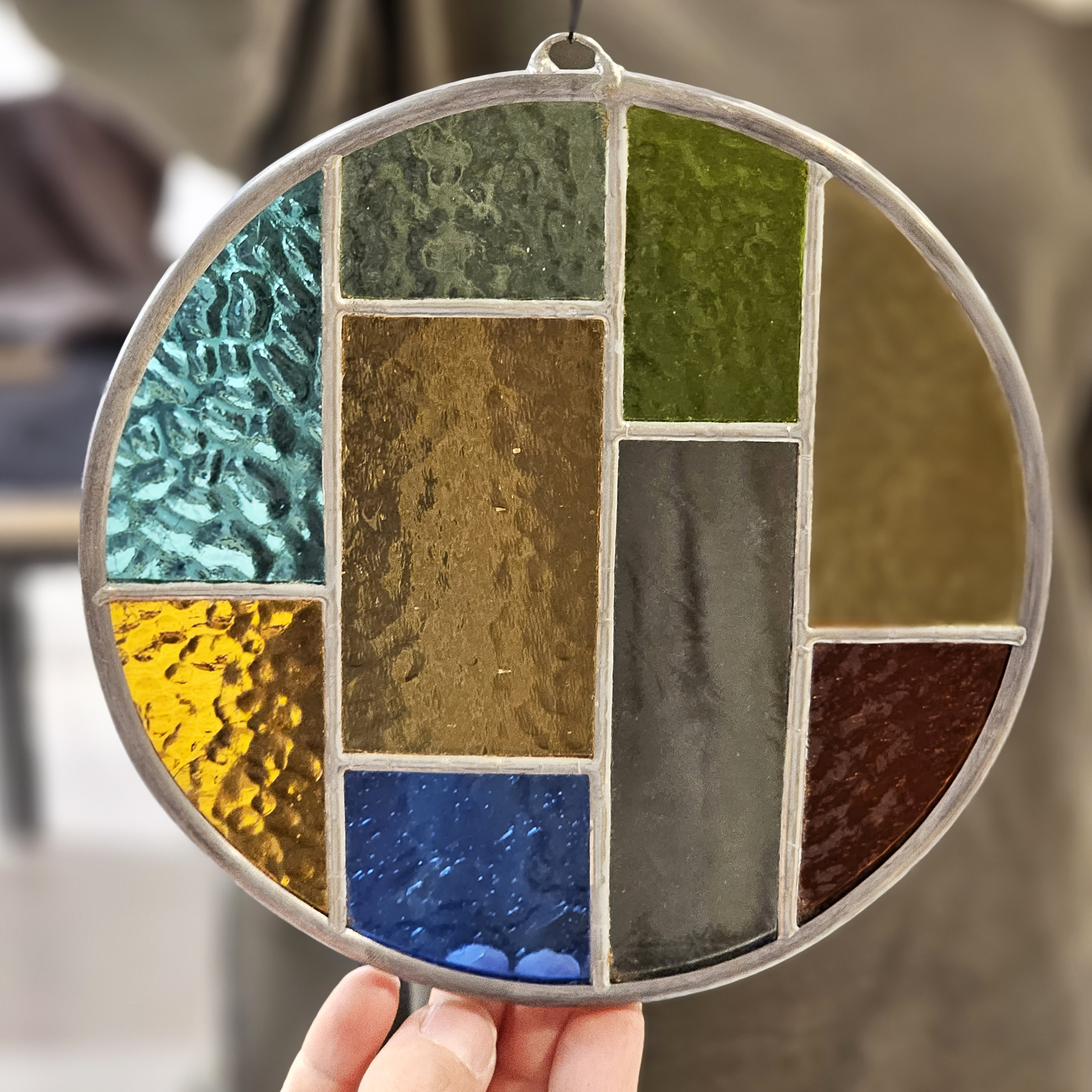 hands holding a stained glass circle filled with different colors with a person standing in background