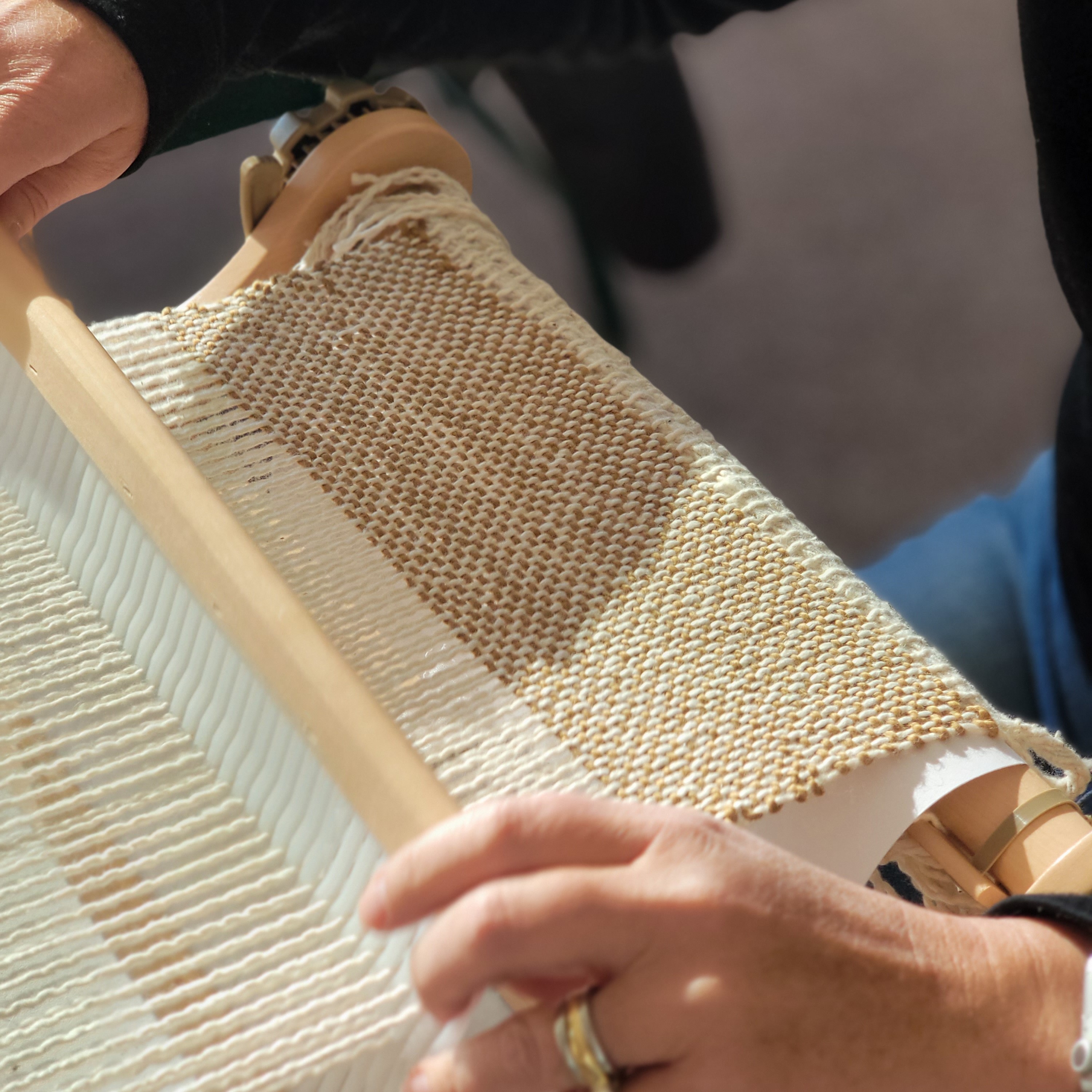 hands working with a rigid heddle loom and weaving tan and cream handwovem fabric