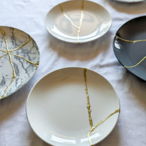 a variety of plates repaired with kintsugi golden repair work resting on white table