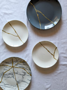 a variety of plates repaired with kintsugi golden repair work resting on white table