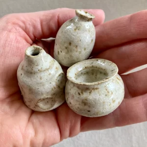 close up of tiny cream colored clay pots in hand
