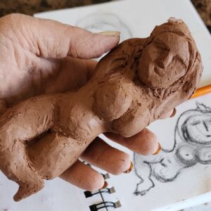 handmade clay figure of a woman sculpted and in hand with a sketch in the background