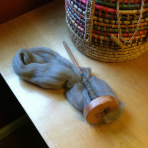 wool fiber being spun into yarn on a drop spindle laying on a table