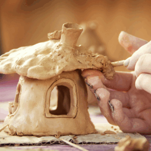 kids hands working with clay as they build a tiny ceramic house